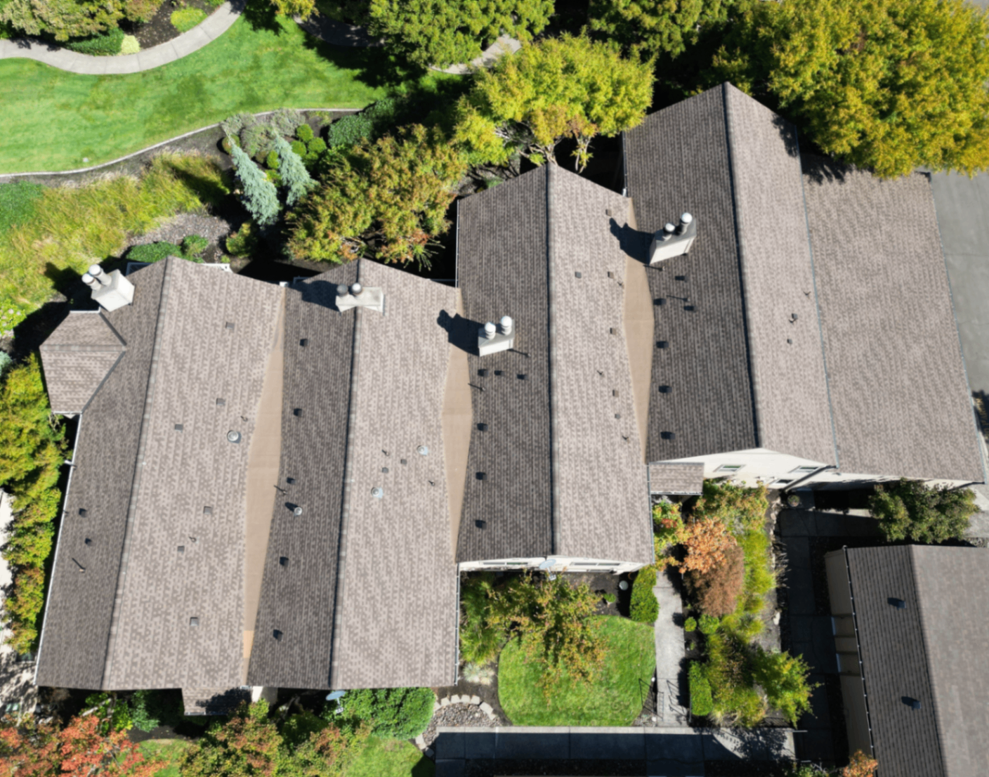 Aerial view of a completed brown shingle residential roof surrounded by landscaping